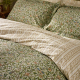 Bird & Pomegranate cotton duvet cover set in herbal green, showing branching floral print with birds and pomegranates alongside the reversible leafy stripe on pillowcases and bedding.