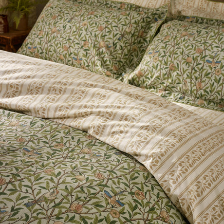 Bird & Pomegranate cotton duvet cover set in herbal green, showing branching floral print with birds and pomegranates alongside the reversible leafy stripe on pillowcases and bedding.