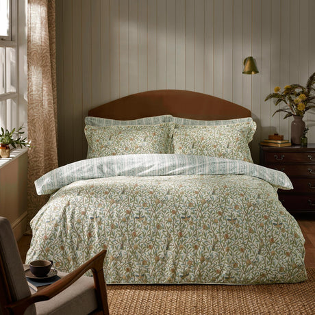 Bird & Pomegranate cotton duvet cover set in sage, shown on a bed with matching pillowcases featuring a green and amber bird and pomegranate print in a bedroom setting.