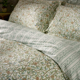Bird & Pomegranate cotton duvet cover set in sage, showing floral bird and pomegranate print reversing to a leafy stripe, with matching pillowcases on a bed.