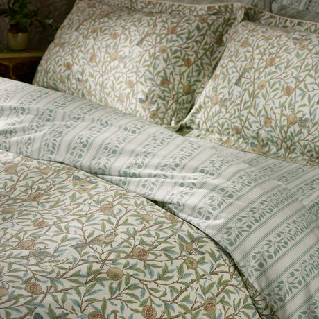 Bird & Pomegranate cotton duvet cover set in sage, showing floral bird and pomegranate print reversing to a leafy stripe, with matching pillowcases on a bed.