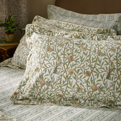 Oxford pillowcases in the Bird & Pomegranate cotton print, sage green branches, birds and pomegranates on cream, styled with striped bedding on a bed.