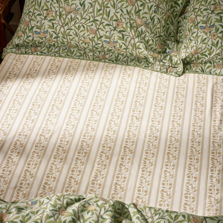 Percale cotton fitted sheet in cream with beige leaf stripe pattern, shown on a bed with matching Bird & Pomegranate floral pillowcases in herbal green.