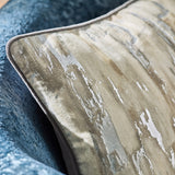 Close-up of the Blocks Velvet Cotton Cushion in silver, featuring a foil-printed abstract vertical stripe design in cream, stone and sandy tones with piped edge, on a blue textured sofa.