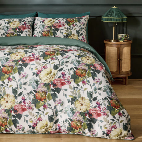 Bloom Cotton Floral Duvet Cover Set in cream with pink, coral and green painterly floral print, shown with matching pillowcases and green reverse on a bed in a dark-walled bedroom.