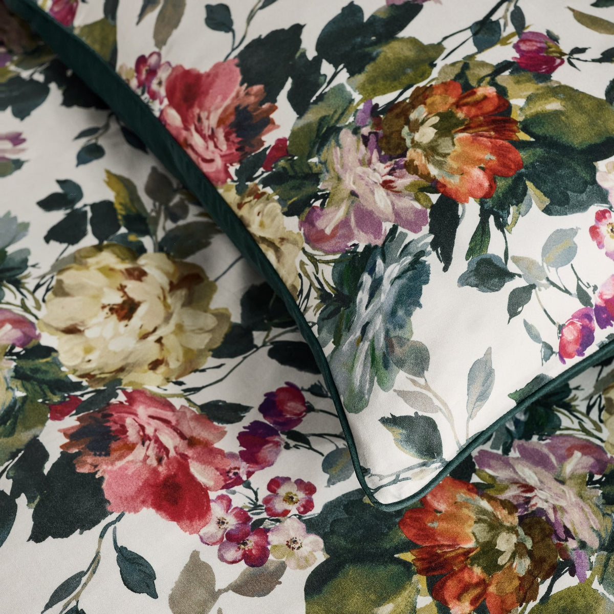 Bloom Cotton Floral Duvet Cover Set close-up showing pink, coral and cream painterly florals with green foliage on a cotton sateen fabric, edged with a solid dark green piping.