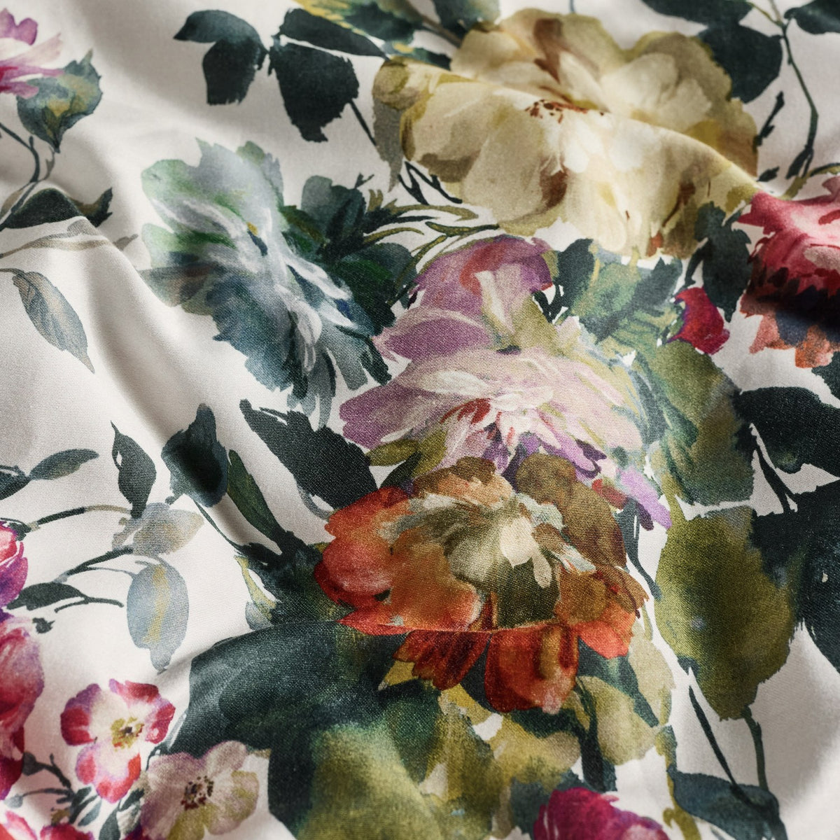 Close-up of the Bloom Cotton Duvet Cover Set fabric, showing a painterly floral print of roses and peonies in cream, pink, coral, purple and green tones on cotton sateen.
