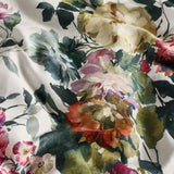 Close-up of the Bloom Cotton Duvet Cover Set fabric, showing a painterly floral print of roses and peonies in cream, pink, coral, purple and green tones on cotton sateen.
