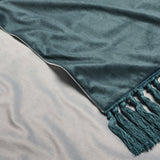 Bloom Plain Velvet Throw in green, close-up of the folded corner showing smooth velvet pile and matching knotted tassel trim, laid on a light grey surface.