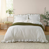 Blousey Cotton Plain Duvet Cover Set in Olive on a bedroom bed, showing a white cotton duvet cover and pillowcases with ruffled edges and fine olive piped trim, styled with an olive throw.