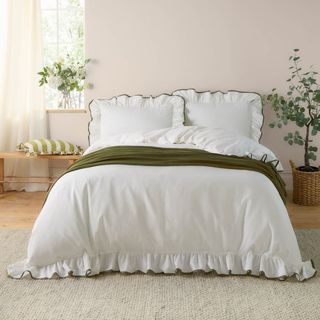 Blousey Cotton Plain Duvet Cover Set in Olive on a bedroom bed, showing a white cotton duvet cover and pillowcases with ruffled edges and fine olive piped trim, styled with an olive throw.