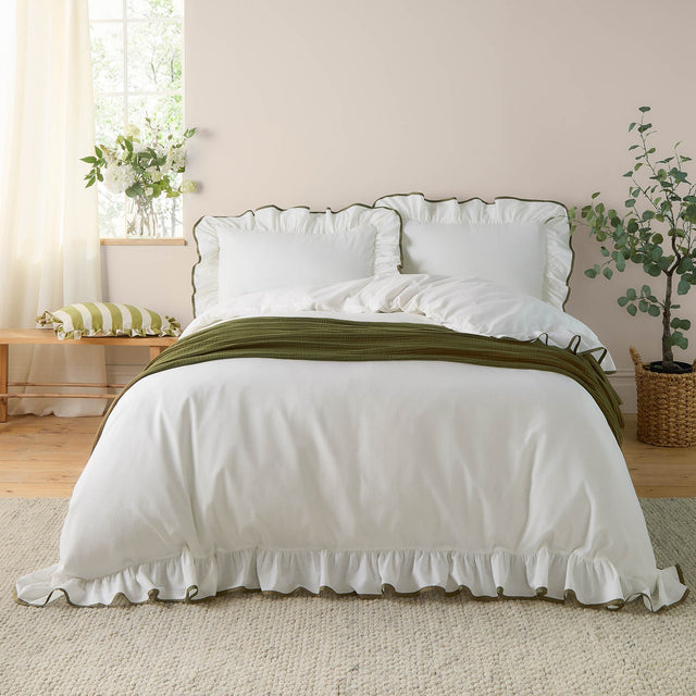 Blousey Cotton Plain Duvet Cover Set in Olive on a bedroom bed, showing a white cotton duvet cover and pillowcases with ruffled edges and fine olive piped trim, styled with an olive throw.
