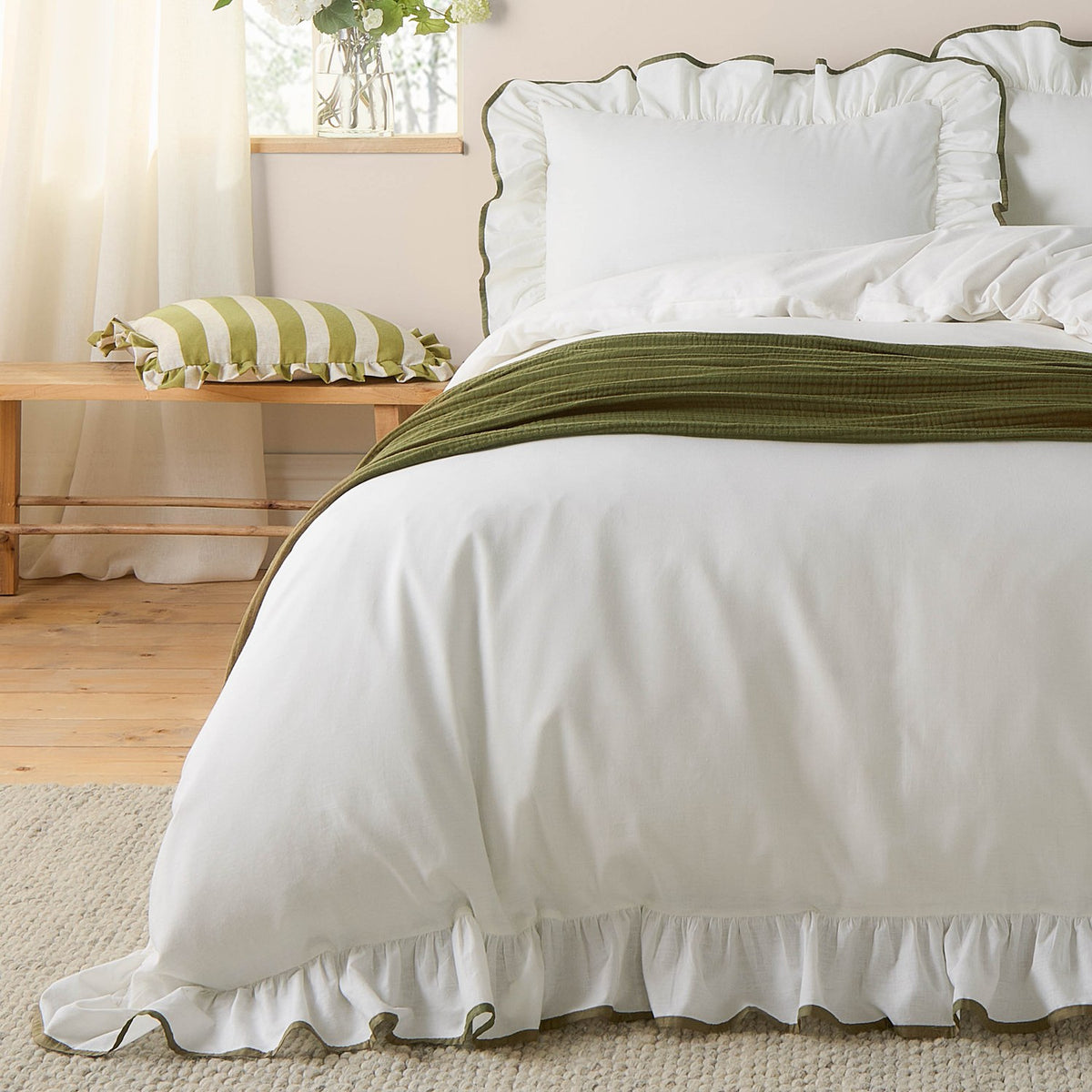 White ruffled-edge cotton pillowcases with olive-green piping styled on a bed, with a striped green and white cushion and olive throw in a bedroom setting.