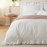 White ruffled cotton pillowcases with pink piped trim styled on a bed, part of the Blousey Plain Cotton Pillowcase Pair in a bedroom setting.