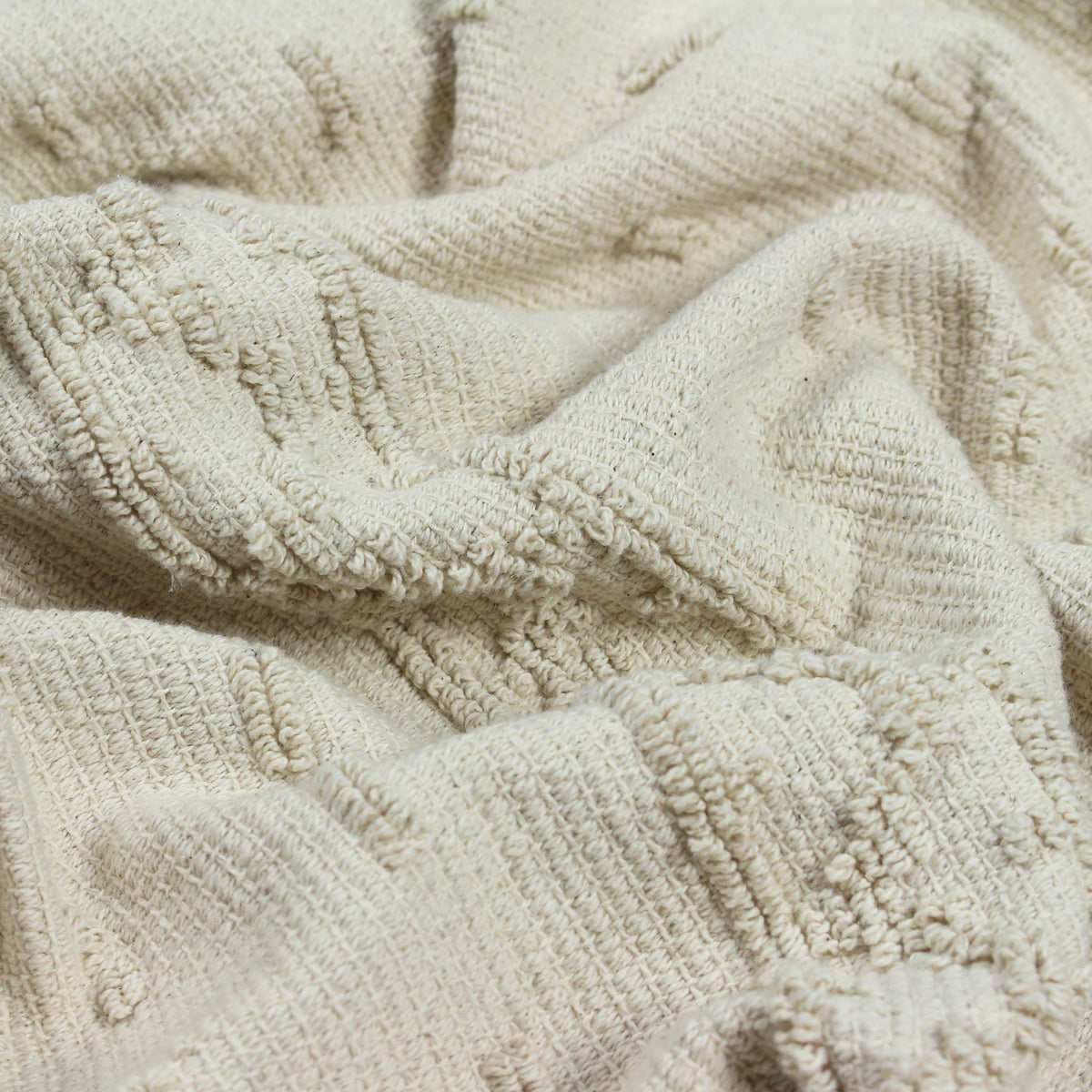 Close-up of the Boho Geometric Cotton Throw in natural cream, showing raised tufted geometric bands woven into the textured cotton fabric.