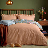 Bootanical Forest reversible duvet cover set styled on a bed, showing the rust-and-cream stripe side with a glimpse of the floral reverse, in a green-walled bedroom setting.