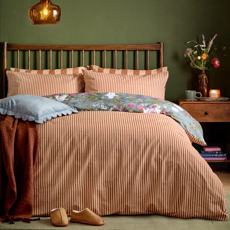 Bootanical Forest reversible duvet cover set styled on a bed, showing the rust-and-cream stripe side with a glimpse of the floral reverse, in a green-walled bedroom setting.