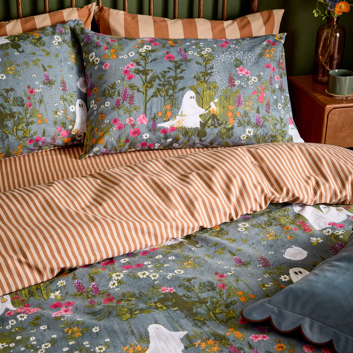 Bootanical Forest Striped Duvet Cover Set in multicolour, styled on a bed with matching pillowcases showing a grey-blue floral scene with white ghost figures, reversing to a rust-and-cream stripe.