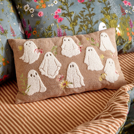 Bootanical Floral Velvet Cushion in Natural, a rectangular beige cushion with tufted white ghost motifs and embroidered floral details, shown on a striped bed setting.