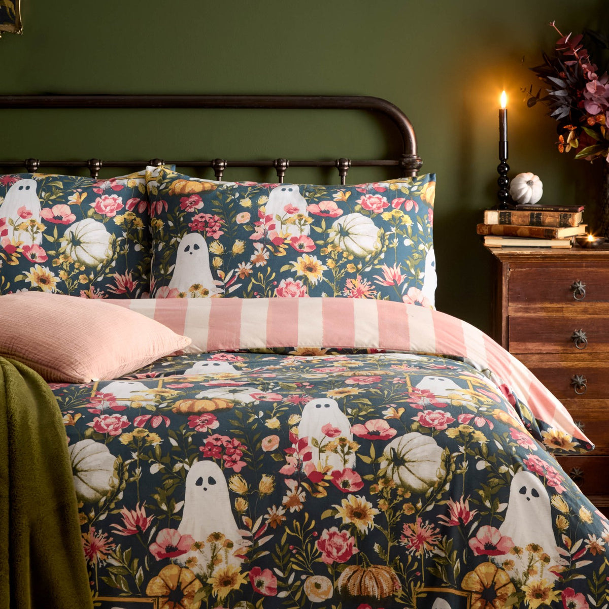 Bootanical reversible duvet cover set on a bed, teal-green polycotton print with ghost motifs, autumnal florals and pale pumpkins, styled with pink and striped pillowcases in a green bedroom setting.