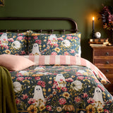 Bootanical reversible duvet cover set on a bed, teal-green polycotton print with ghost motifs, autumnal florals and pale pumpkins, styled with pink and striped pillowcases in a green bedroom setting.