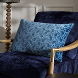 Boteh Velvet Cotton Cushion in True Blue/Navy paisley print, rectangular shape, shown on a navy velvet armchair beside a wooden floor lamp.
