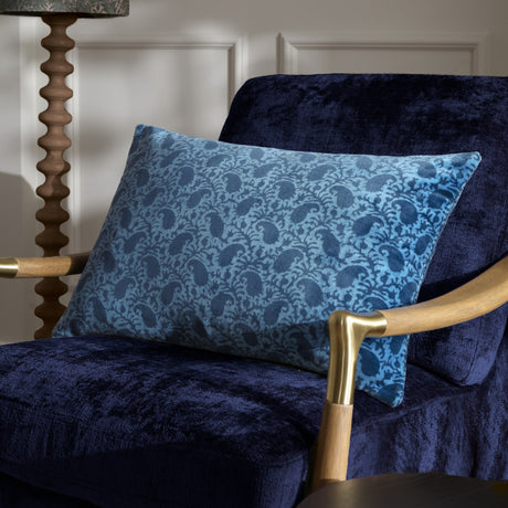 Boteh Velvet Cotton Cushion in True Blue/Navy paisley print, rectangular shape, shown on a navy velvet armchair beside a wooden floor lamp.