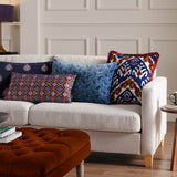 Boteh Velvet Cotton Cushion in True Blue/Navy paisley print, rectangular, shown on a beige sofa among other patterned cushions in a living room setting.