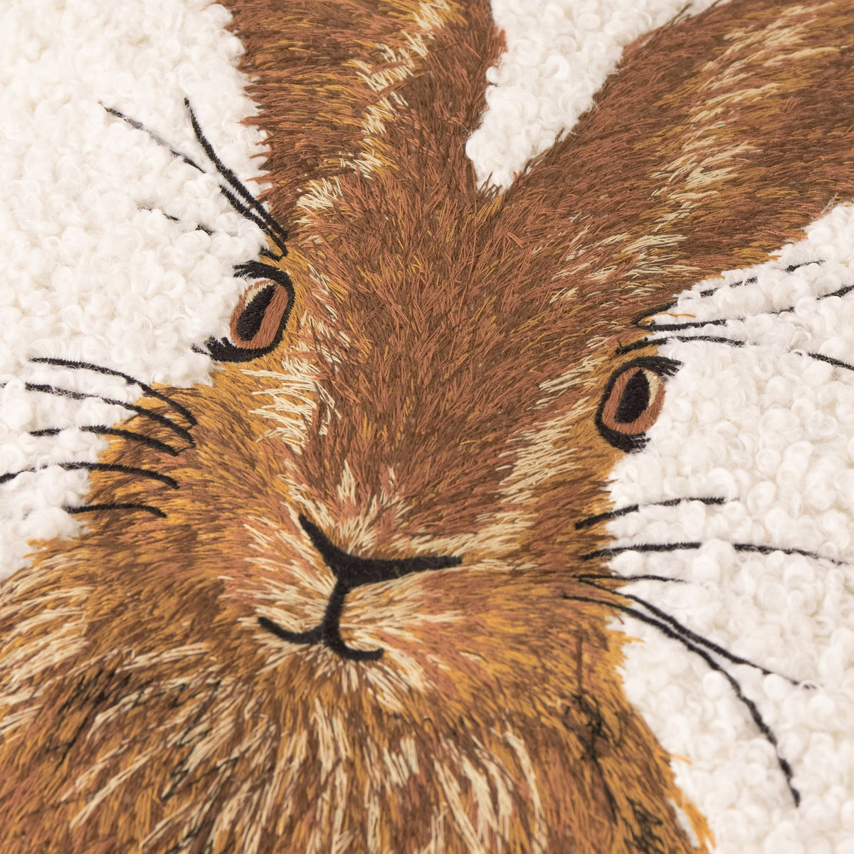 Close-up of the Boucle Hare Animal Polyester Cushion in natural, showing an embroidered hare's face in brown and tan tones on textured cream boucle fabric.