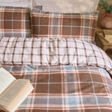 Braemar Check Cotton Reversible Duvet Cover Set in Chocolate/Blue on a bed with matching pillowcases, reverse side in cream and brown check, styled with a bedside table and open book.