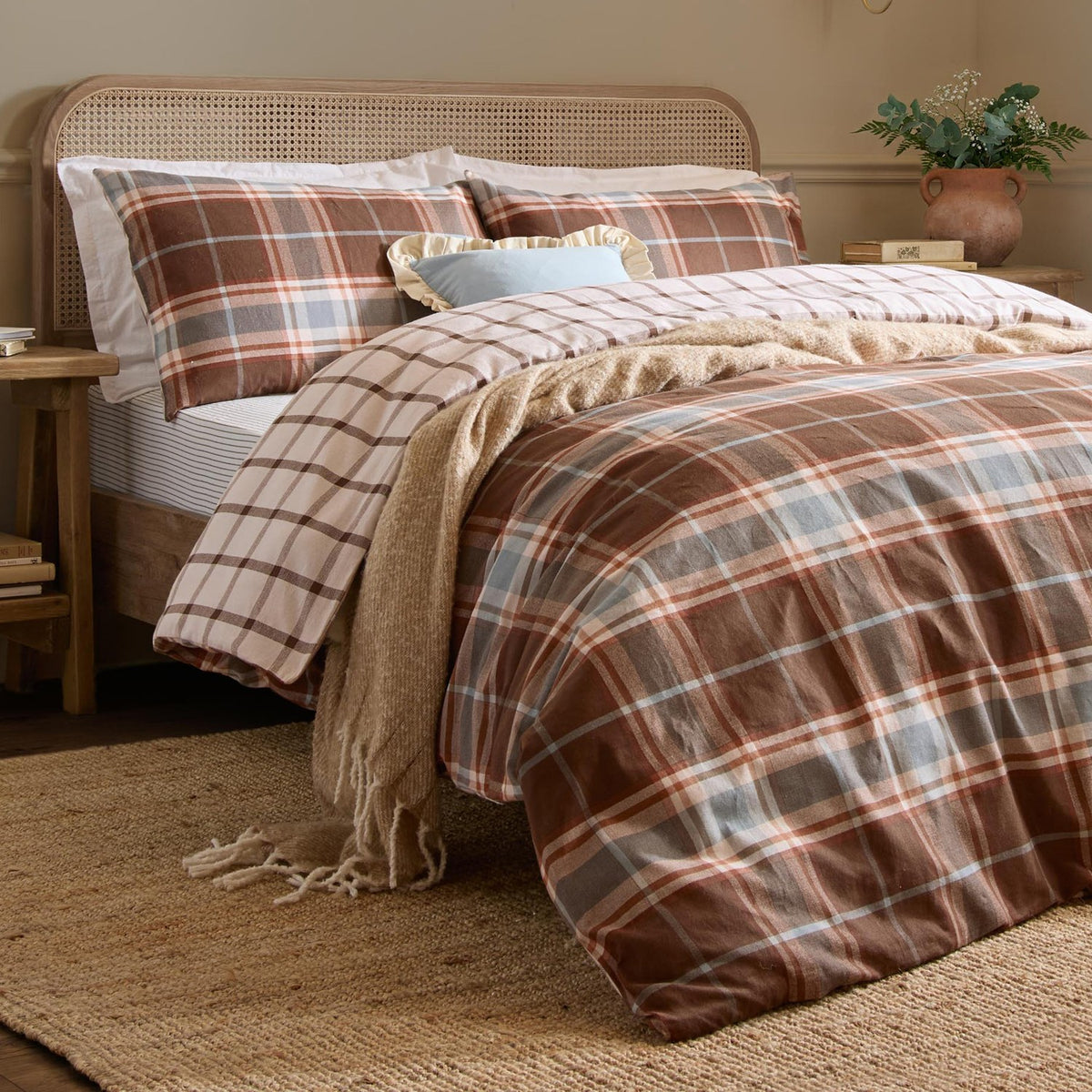Braemar Check Cotton Reversible Duvet Cover Set in chocolate and blue plaid, styled on a bed with matching pillowcases, a cane headboard, and a knitted throw in a bedroom setting.