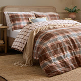 Braemar Check Cotton Reversible Duvet Cover Set in chocolate and blue plaid, styled on a bed with matching pillowcases, a cane headboard, and a knitted throw in a bedroom setting.