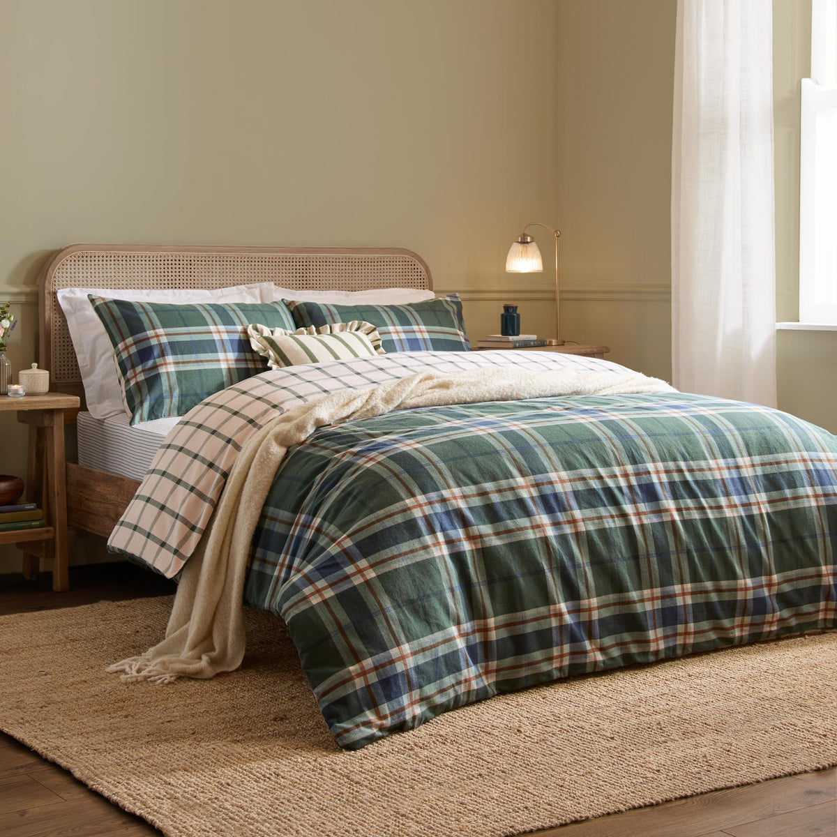 Braemar Check Cotton Reversible Duvet Cover Set in Forest/Navy tartan-style plaid, styled on a bed with matching pillowcases in a bedroom setting with rattan headboard and cream throw.