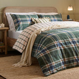 Braemar Check Cotton Reversible Duvet Cover Set in Forest/Navy tartan-style plaid, shown on a bed with matching pillowcases, cream ruffled cushion, and beige throw in a bedroom setting.