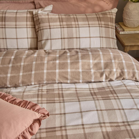 Braemar Check Cotton Reversible Duvet Cover Set in natural beige and cream tartan-inspired check, shown with matching pillowcases on a bed beside pink bedding and a wooden nightstand.
