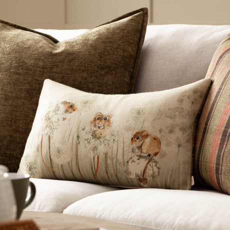 Bramble Mice rectangular scatter cushion in oatmeal fabric with hand-painted mice among meadow grasses, shown on a sofa with striped and olive cushions.