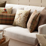 Bramble Hare Reversible Polyester Cushion in beige and green with a hand-painted hare and botanical print, styled on a cream sofa with plaid and pheasant-print cushions.