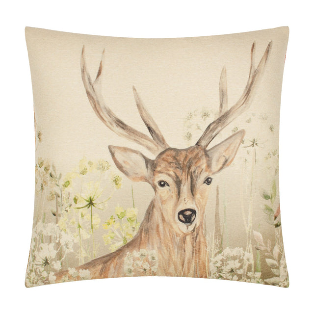 Square polyester cushion with a hand-painted stag print facing forward, antlers rising above meadow flowers and seed heads on a cream and brown natural background.