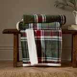 Braemarcheck red and green tartan polyester throw, partly folded on a wooden bench to reveal the cream Sherpa fleece reverse, in a living room setting.