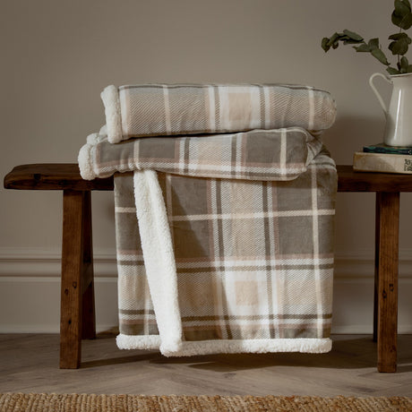 Braemar check polyester throw in grey and natural tartan with Sherpa fleece reverse, folded on a wooden bench in a living room setting.