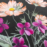 Close-up of the Braywick velvet cushion in black, showing a printed wildflower design with coral cosmos, magenta blooms and golden centres against the dark fabric ground.