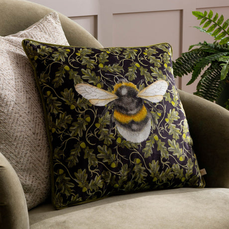 Braywick Animal Velvet Cushion in Bee design, a 43 x 43cm square cushion with a bumblebee motif on a dark green oak leaf and acorn print, shown on an armchair.