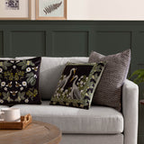 Braywick Animal Velvet Cushion in black with printed crane design and floral vine border, styled on a grey sofa alongside bee-print and herringbone cushions.