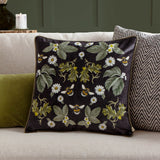 Braywick Animal Velvet Cushion in black with mirrored floral design of daisies, leaves, acorns and bumblebees, shown on a sofa in a living room setting.