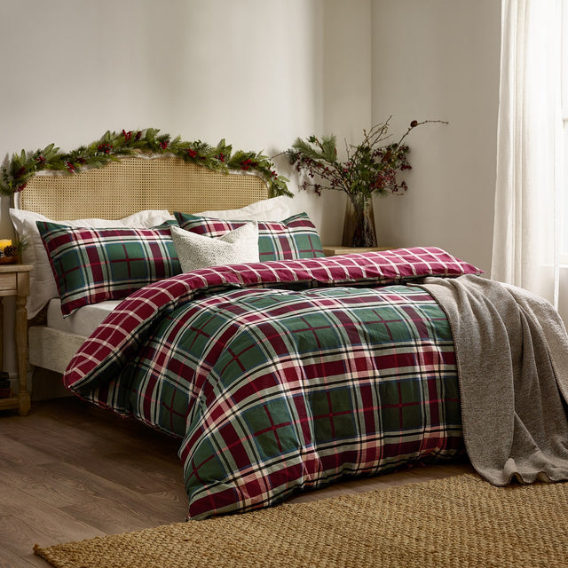 Braemar Check Cotton Reversible Duvet Cover Set in Berry/Pine on a bed with matching pillowcases, green tartan check reverse, cream cushion, and grey throw in a bedroom setting.