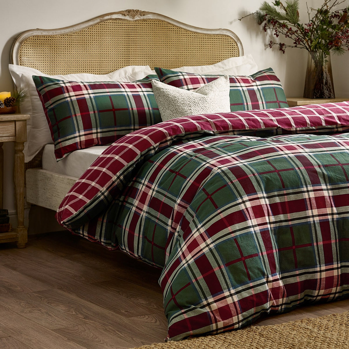 Braemar Check Cotton Reversible Duvet Cover Set in Berry/Pine tartan on a bed with matching pillowcases and a cane headboard in a bedroom setting.