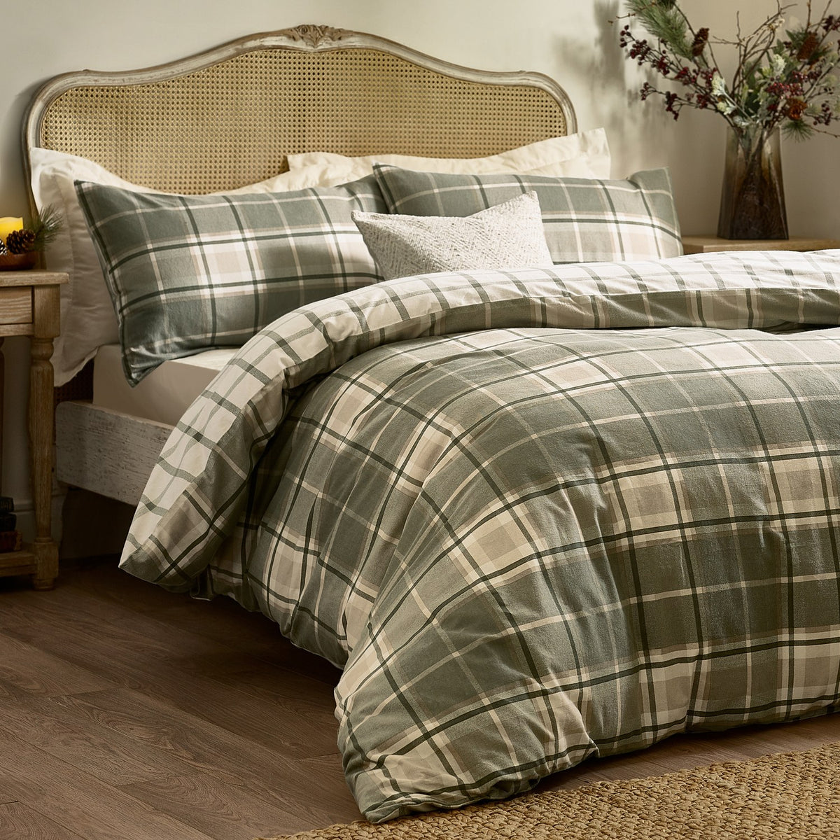 Braemar Check cotton reversible duvet cover set in green and natural tartan-style print, shown styled on a bed with matching pillowcases against a rattan headboard.