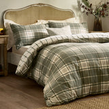 Braemar Check cotton reversible duvet cover set in green and natural tartan-style print, shown styled on a bed with matching pillowcases against a rattan headboard.