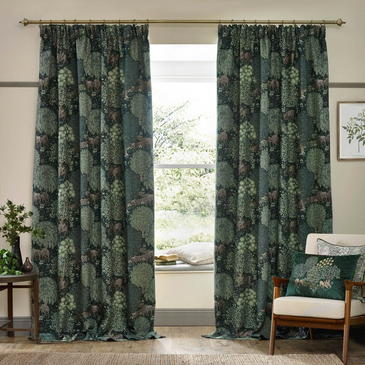 Brook Jacquard pencil pleat curtains in forest green with woven woodland deer and tree design, hung on a brass pole in a living room beside a window seat.
