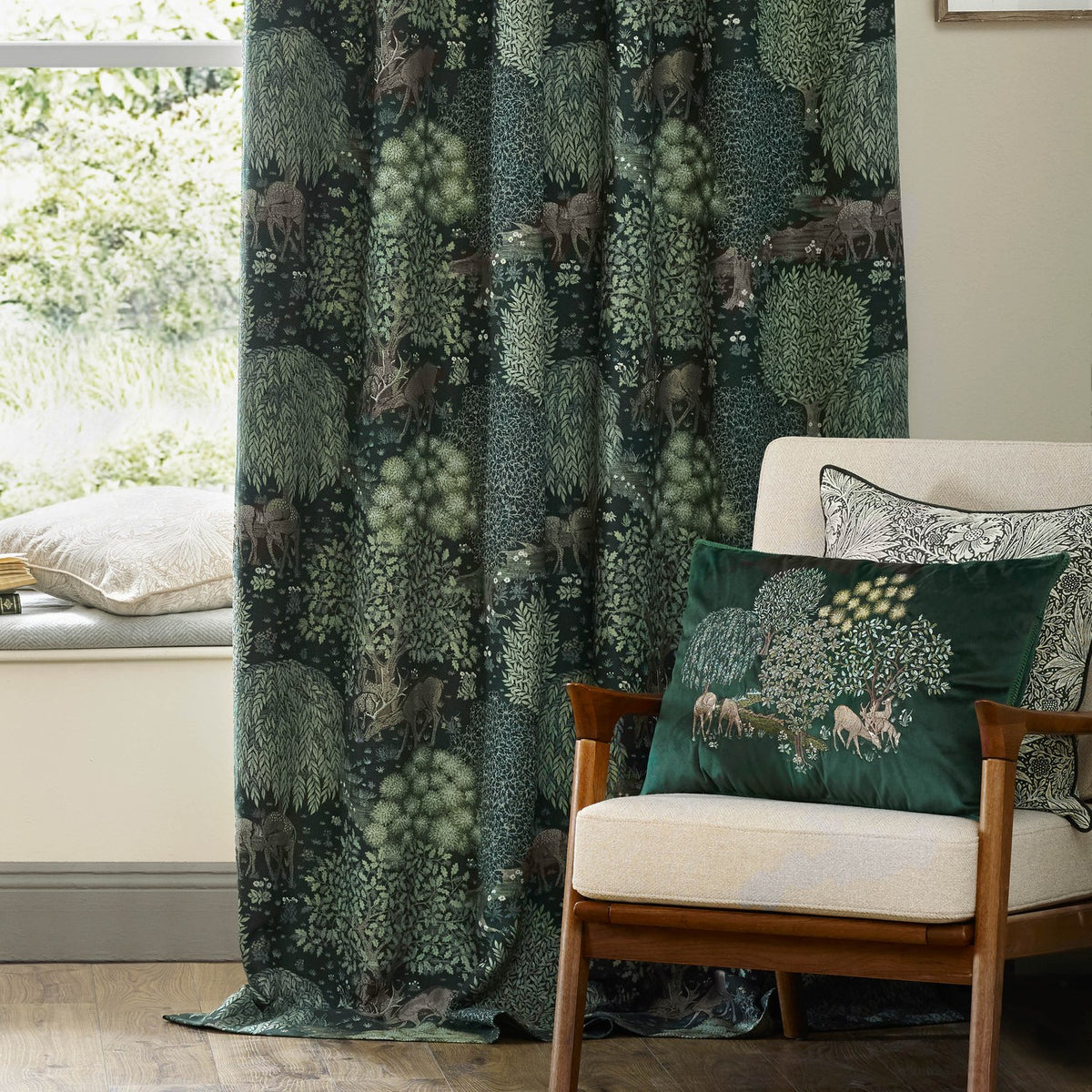 Brook Jacquard Polyester Pencil Pleat Curtains in Forest Green with woven woodland deer and tree motif, shown draped by a window beside a matching cushion on an armchair.
